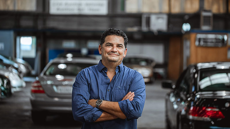 Man crossing his arms looking at the camera standing in a garage full of cars.