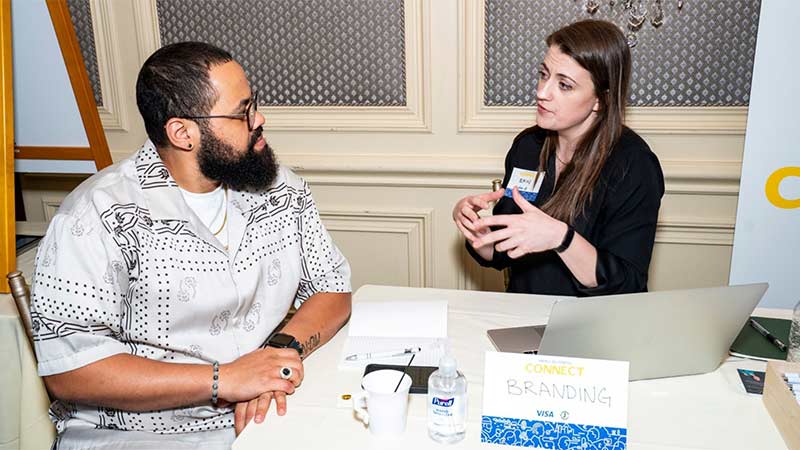 Small business owner Derrick Valerio sits at a table getting advice from branding expert Erin Choplin