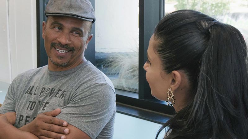 A man and a woman talk in front of a window