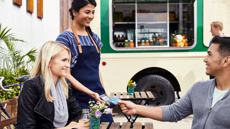 A young man taps to pay with a Visa card at a food truck.