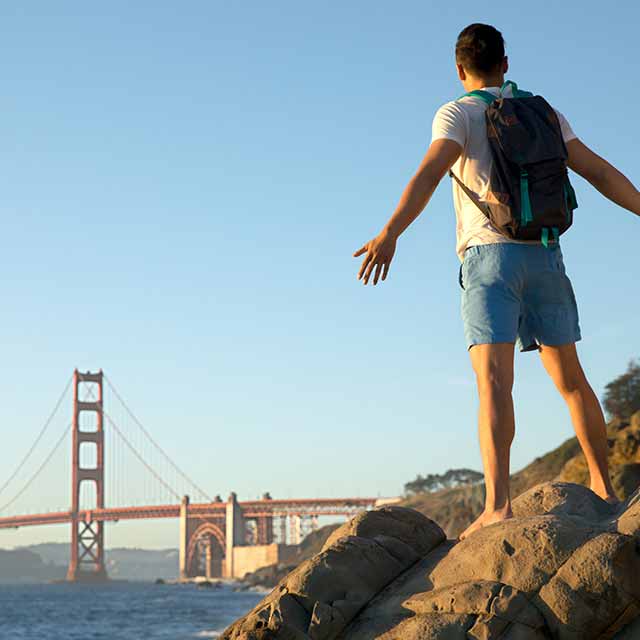 A traveler stands on a cliff that overlooks the Golden Gate Bridge in San Francisco.
