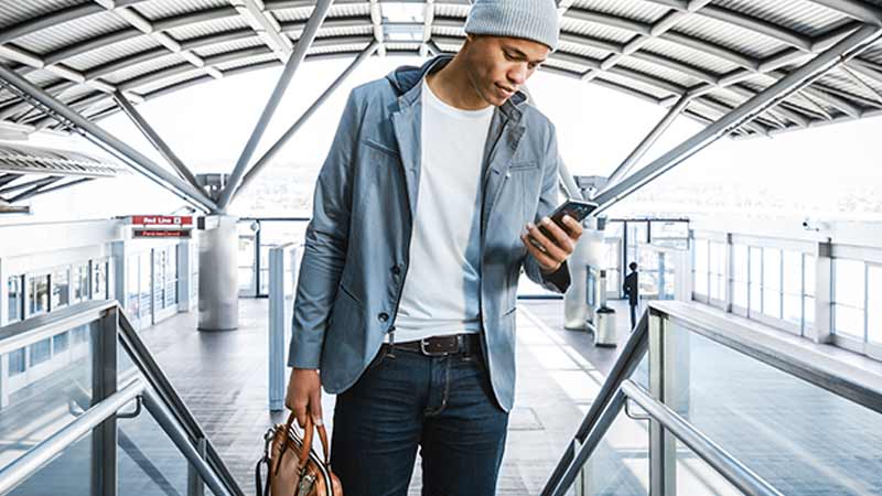 Man viewing his mobile phone at the top of stairs in an airport.