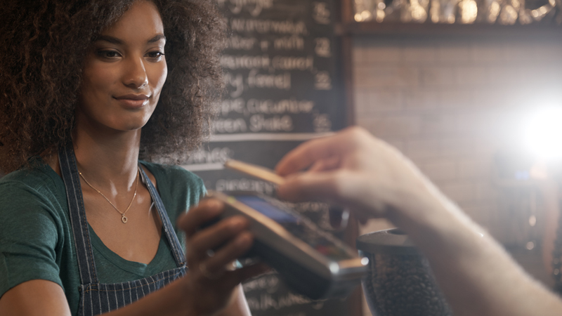 A barista accepting a customer payment via a smart phone at a POS device. A barista accepting a customer payment via a smart phone at a POS device.
