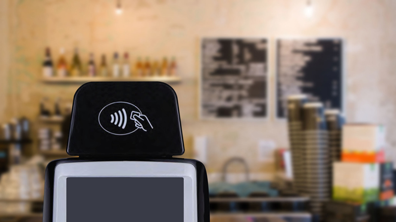 Closeup of a POS system in a coffee shop displaying the Tap to Pay logo.