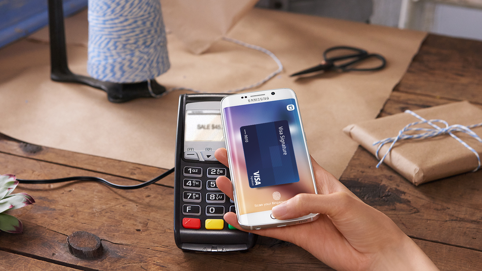 A hand holding a mobile phone over a POS device making a Samsung Pay payment.