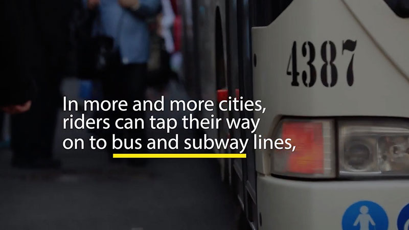 Close-up of city bus with text overlay reading "In more and more cities, riders can tap their way on to bus and subway lines"