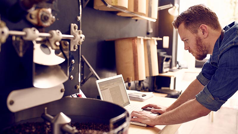 Man leaning over desk working on laptop computer