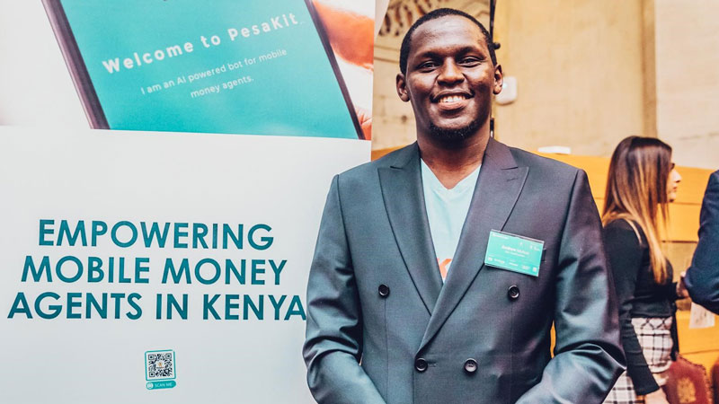 PesaKit founder and CEO Andrew Mutua stands in front of a sign for his company, which offers affordable e-float loans to mobile money agents in Kenya. 