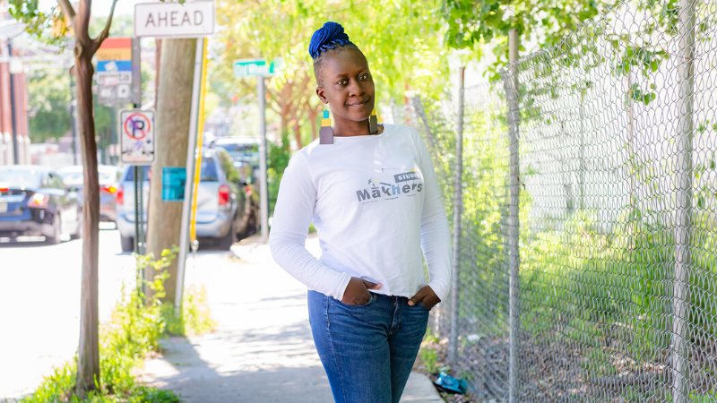 Image of woman standing outside in front of a fence with her hands in her pockets