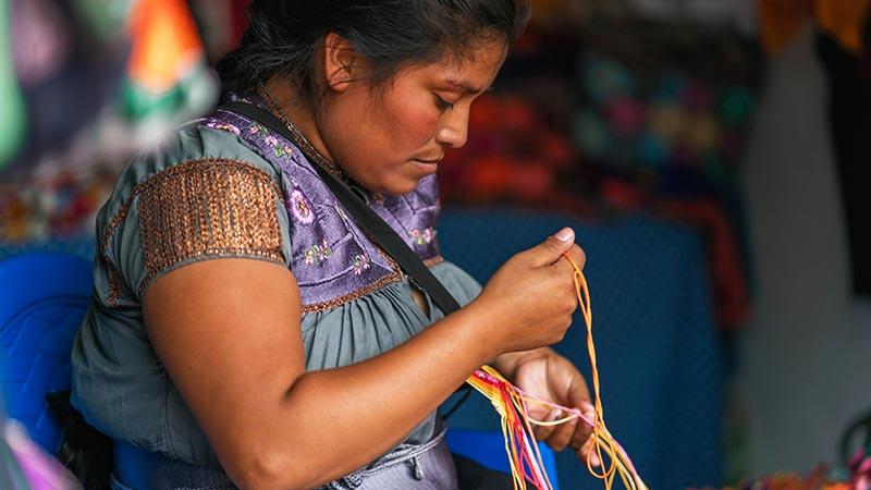 Small business owner in Central America crafting with colorful threads.