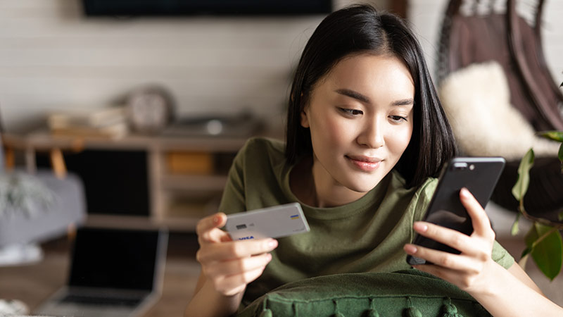 Young asian woman buying from online shop, using mobile phone and credit card, shopping from home
