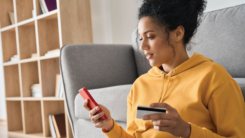 woman wearing yellow hoodie entering her card information into her smartphone