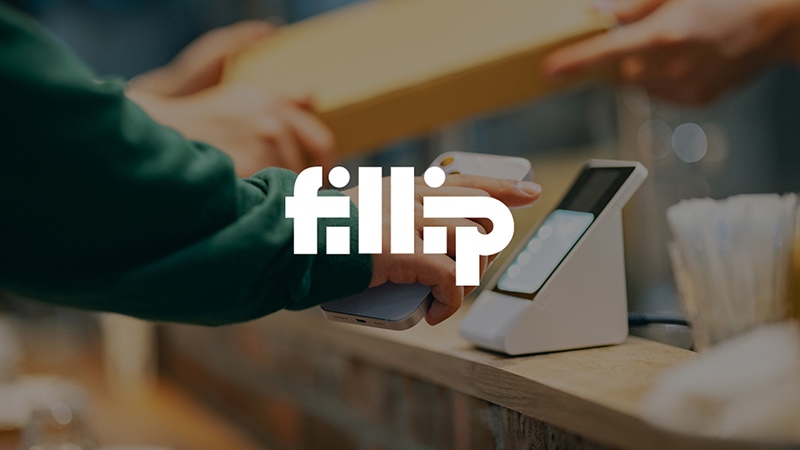 A person in a green, long sleeve shirt tapping a white smartphone to an in-store POS with the Fillip logo superimposed.