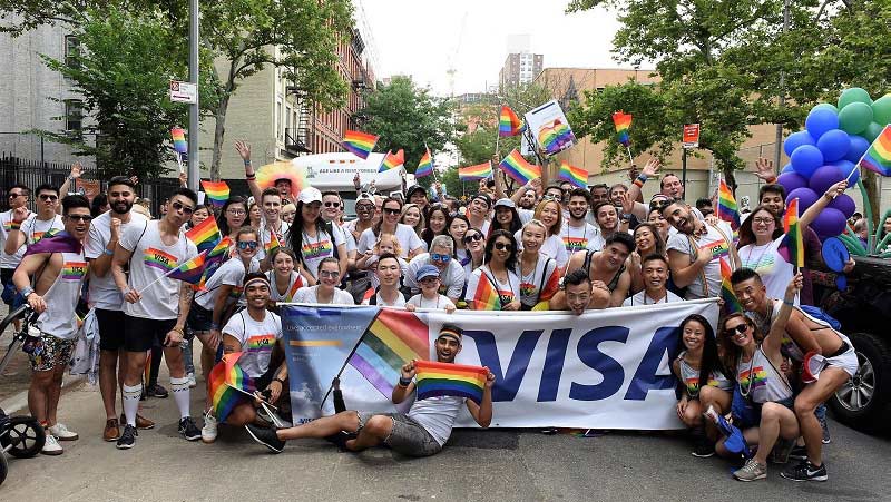 Large group of Visa group of employees standing in behind Visa banner at Pride Parade