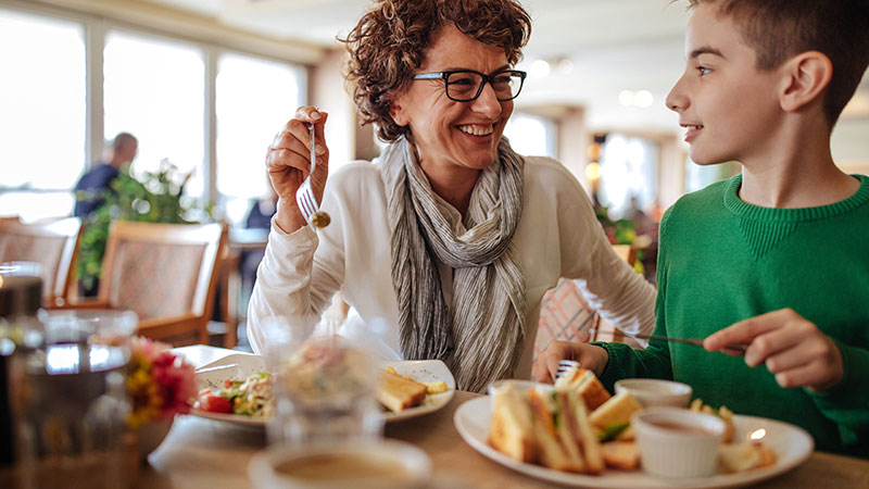 A woman and boy smiling and enjoying their food at a restaurant. A woman and boy smiling and enjoying their food at a restaurant.