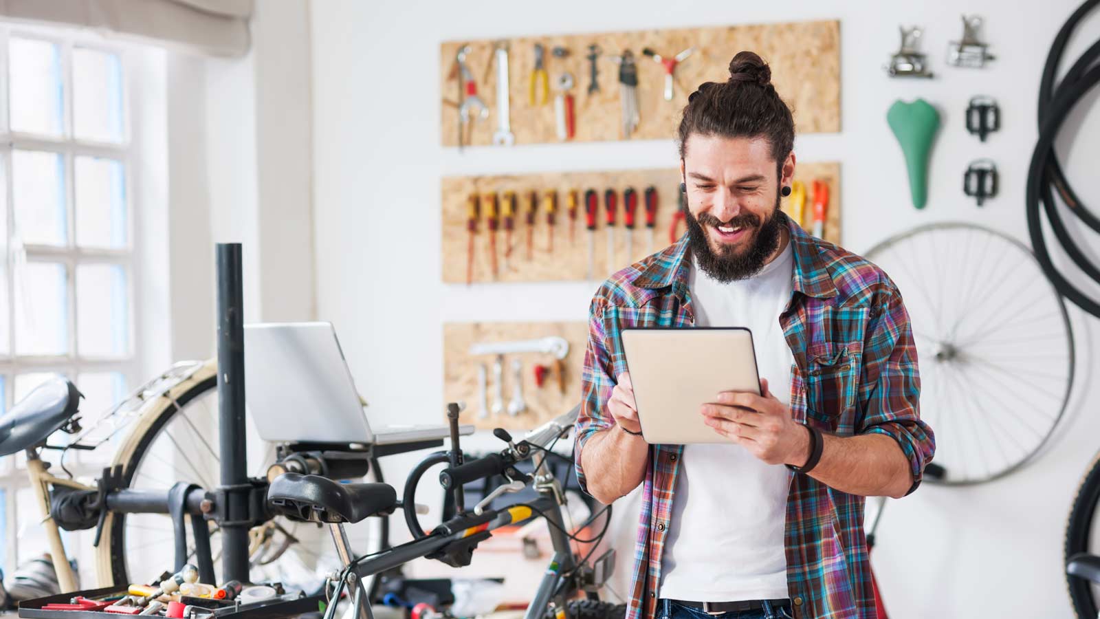 In a bike shop, a bearded young employee uses a tablet.