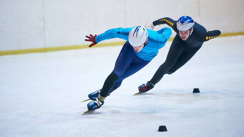 Two male Olympians make a tight turn on an ice skating rink. Two male Olympians make a tight turn on an ice skating rink.