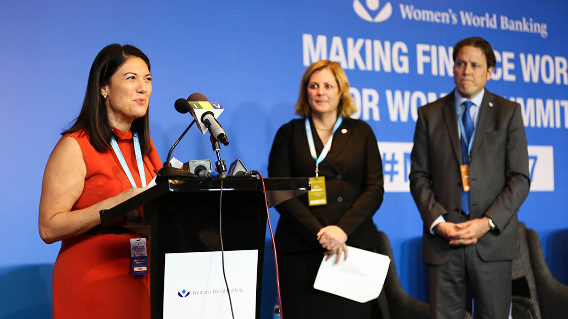 At a Women’s World Banking event, a female speaker, makes an announcement at a podium. 