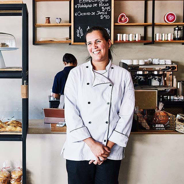 Female in white bakers coat inside a bakery.
