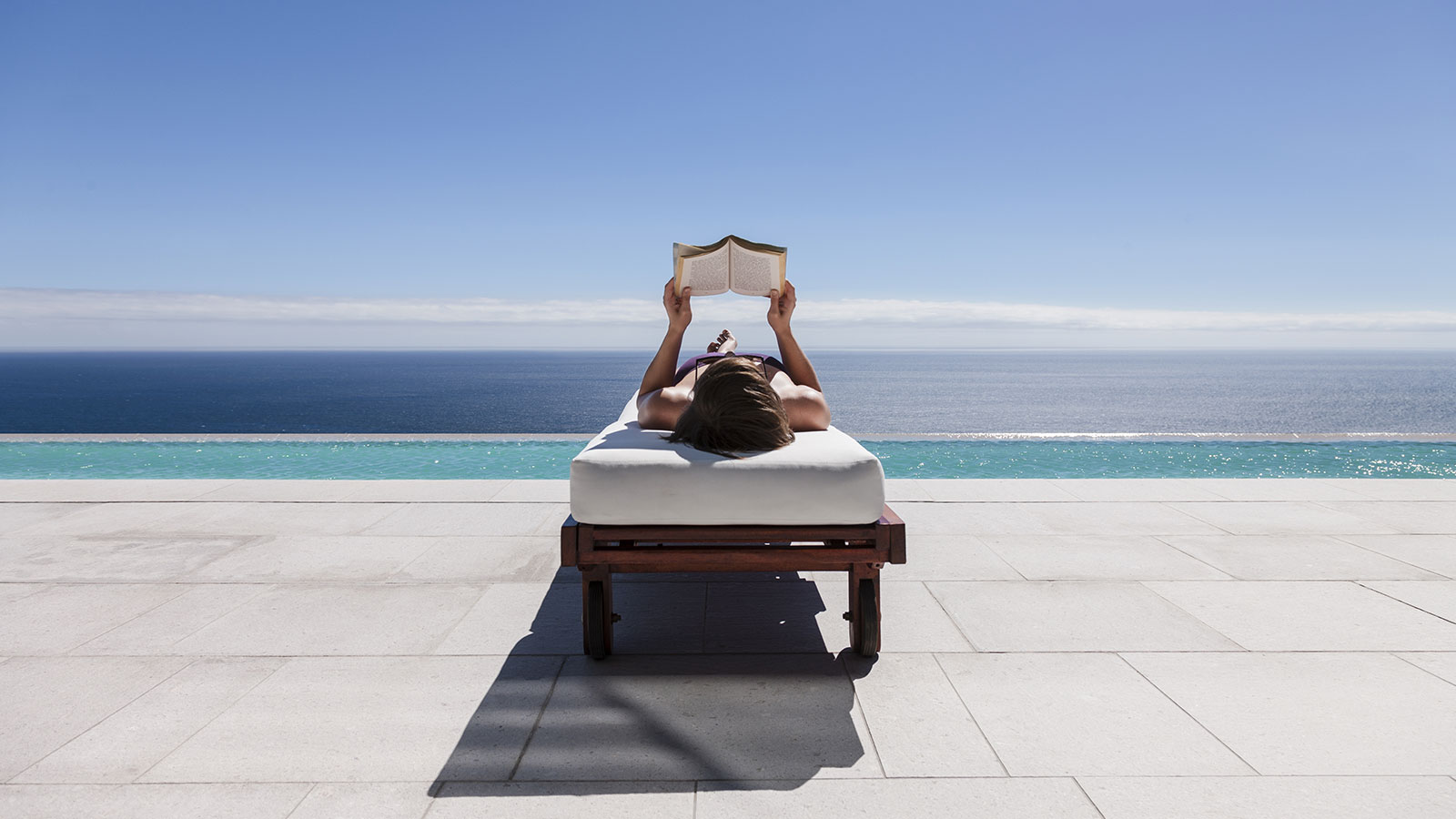 A woman reading a book while reclining on a lounge chair overlooking the beach. A woman reading a book while reclining on a lounge chair overlooking the beach.