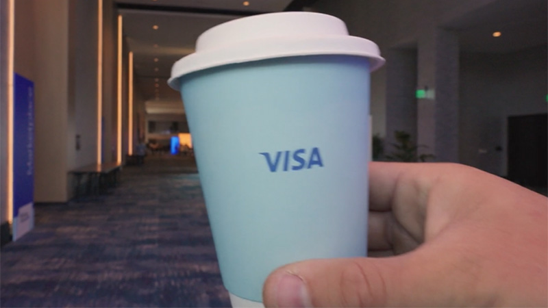 Hand holding a coffee cup with the Visa logo on it.