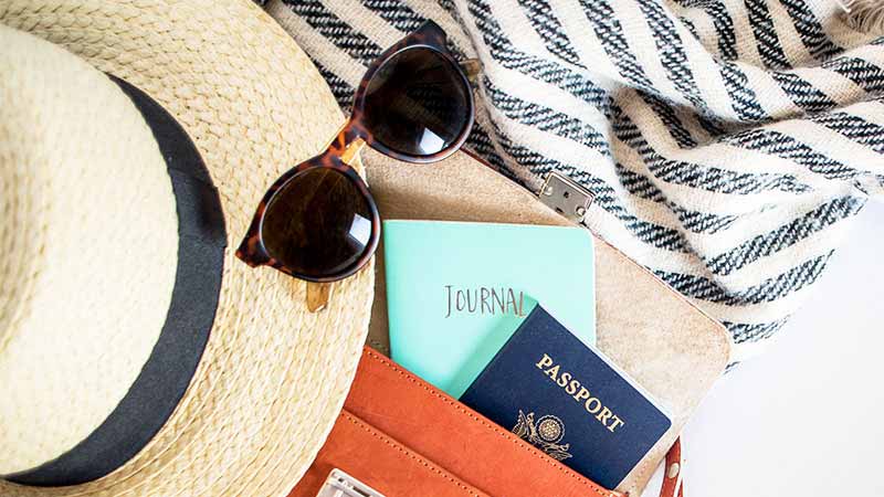A closeup of travel essentials, passport, sun glasses and hat.