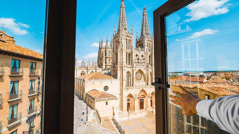 A man looks out his hotel room window towards a historic cathedral in Spain. 