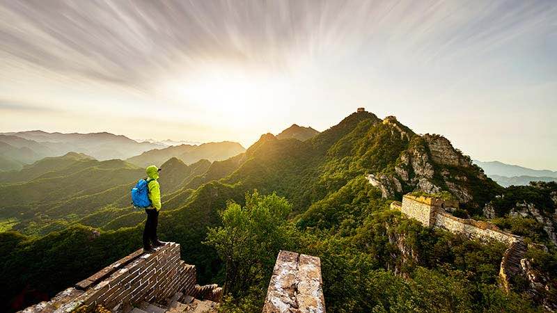 A traveler wearing a backpack looks out over the Great Wall of China.