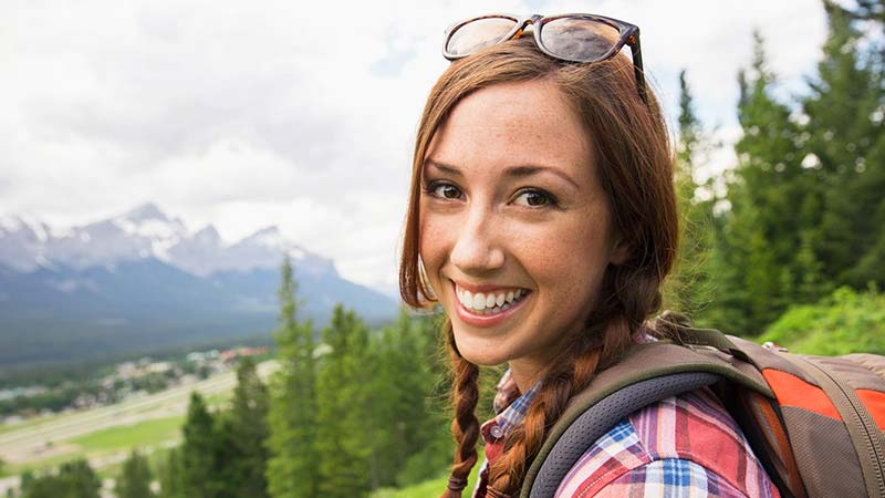 A happy backpacker, in a magnificent outdoor setting, smiles at the camera.
