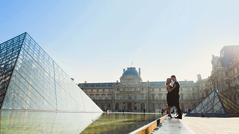 A romantic couple embrace outside of the Louvre museum in Paris.