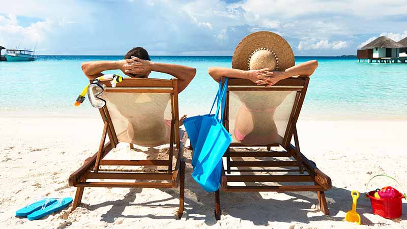 Couple rest in lounge chairs on the beach. 