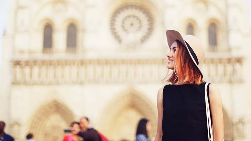 A stylish young woman stands in front of Notre Dame cathedral.