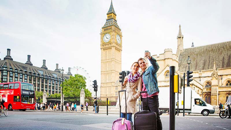A young couple take a selfie in front of a historical building in London.
