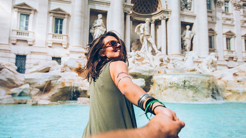 A smiling woman in front of Trevi Fountain in Rome, Italy.