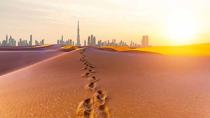 Footprints through the desert in Dubai with city skyline in distance.